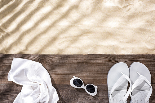 top view of sand with copy space and white towel, retro sunglasses and flip flops on wooden brown board
