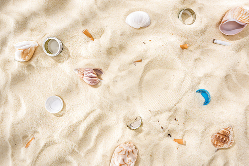 top view of seashells, bottle caps, scattered cigarette butts, plastic bottle caps on sand
