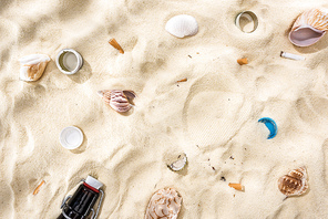 top view of seashells, bottle caps, scattered cigarette butts and glass bottle on sand