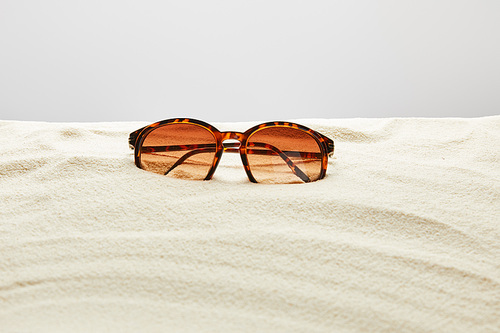 brown stylish sunglasses on sand on grey background