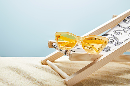 yellow sunglasses and deck chair on sand on blue background