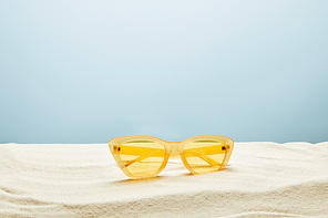 yellow stylish sunglasses on sand on blue background