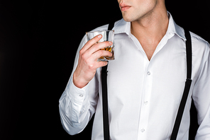 cropped view of man in white shirt and suspenders holding glass of whiskey isolated on black