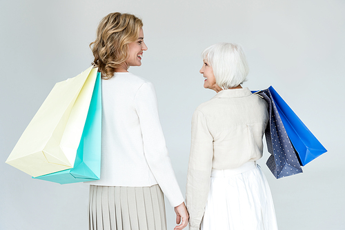 back view of smiling mother and daughter holding shopping bags isolated on grey