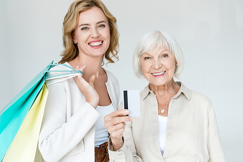 smiling mother with credit card and daughter holding shopping bags isolated on grey