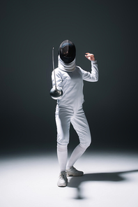 Fencer in fencing mask and suit training under spotlight on black background