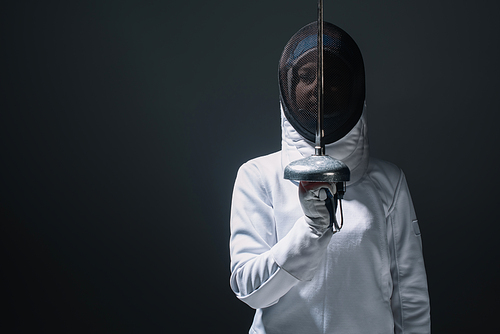 Fencer holding rapier near fencing mask isolated on black