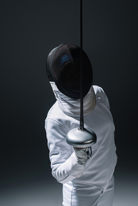 Fencer in fencing mask holding rapier on black background