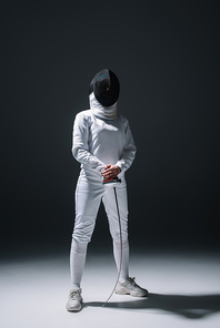 Fencer in fencing mask holding rapier under spotlight on black background