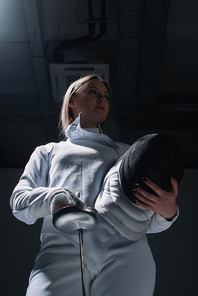 Low angle view of beautiful fencer holding rapier and fencing mask
