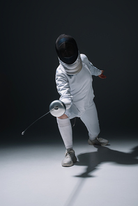 Fencer in fencing mask holding rapier while training on white surface on black background