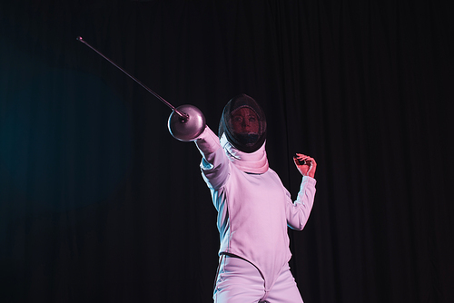 Low angle view of fencer training with rapier isolated on black