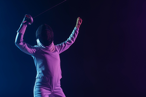 Fencer in fencing mask holding rapier while showing yes gesture isolated on black