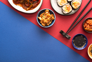 top view of bowls and plates with korean kimchi and kimbap on blue and crimson