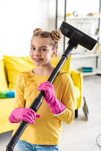 Cute kid in rubber gloves with vacuum cleaner smiling and  in living room