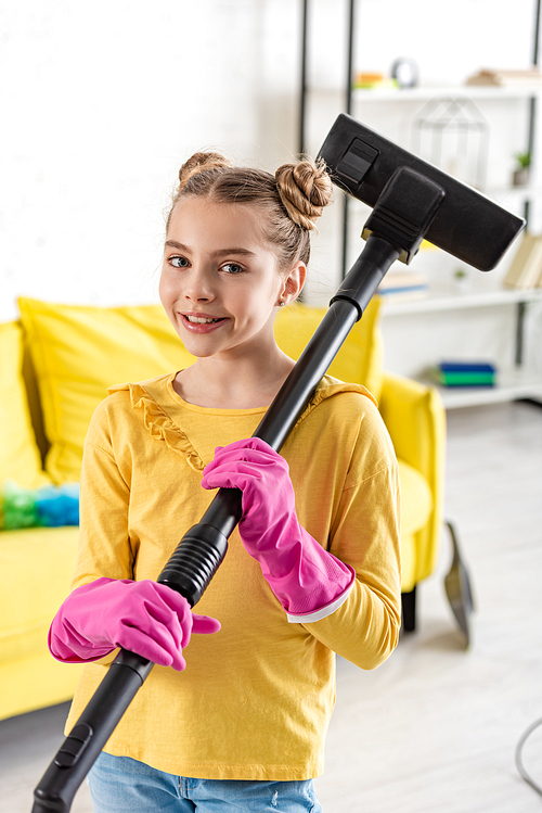 Cute kid in rubber gloves with vacuum cleaner smiling and  in living room