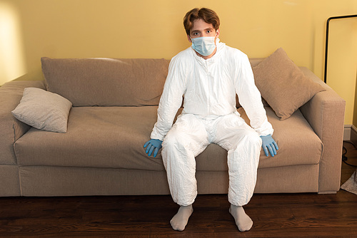 Man in medical mask, hazmat suit and latex gloves  in living room