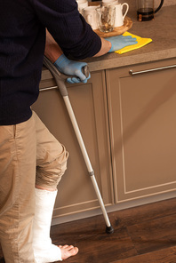 Cropped view of man with plaster bandage on leg cleaning worktop in kitchen