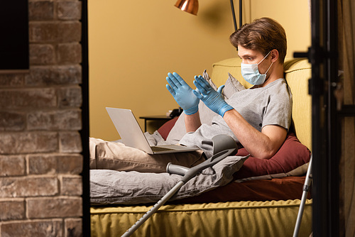 Selective focus of disabled man in medical mask and latex gloves having video chat on laptop in bedroom