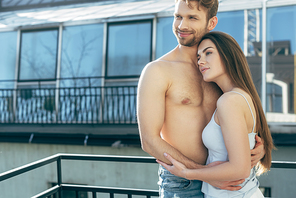 happy and shirtless man hugging with attractive woman on balcony