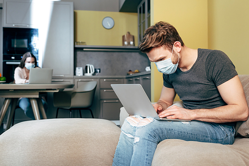 selective focus of freelancer in medical mask working from home near girlfriend