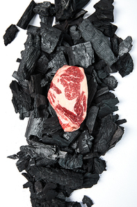 top view of fresh raw steak on black coals on white background