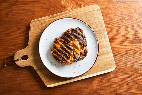 top view of fresh grilled steak on plate on cutting board on wooden table