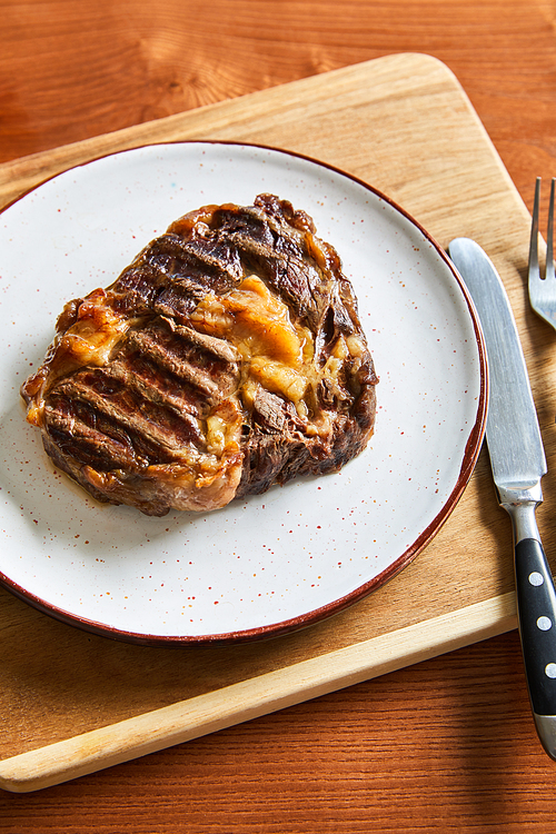 fresh grilled steak on plate on cutting board with cutlery on wooden table