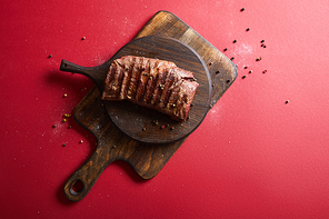 top view of tasty grilled steak served on wooden boards on red background with pepper and salt
