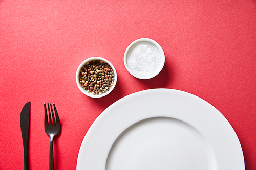 top view of empty round plate with cutlery and salt and pepper in bowls on red background