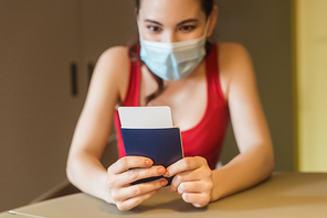 selective focus of young woman in medical mask holding passport and air ticket
