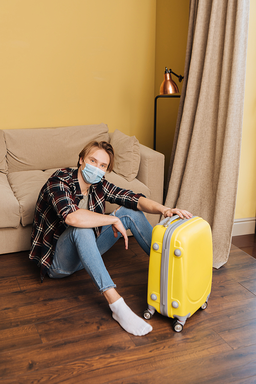 young man in medical mask sitting on floor near baggage, end of quarantine concept