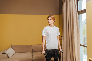 handsome young man exercising with dumbbells in living room, end of quarantine concept