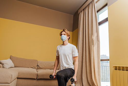 man in medical mask exercising with dumbbells in living room