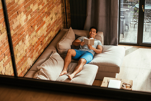 mixed race man reading book while chilling on sofa during quarantine
