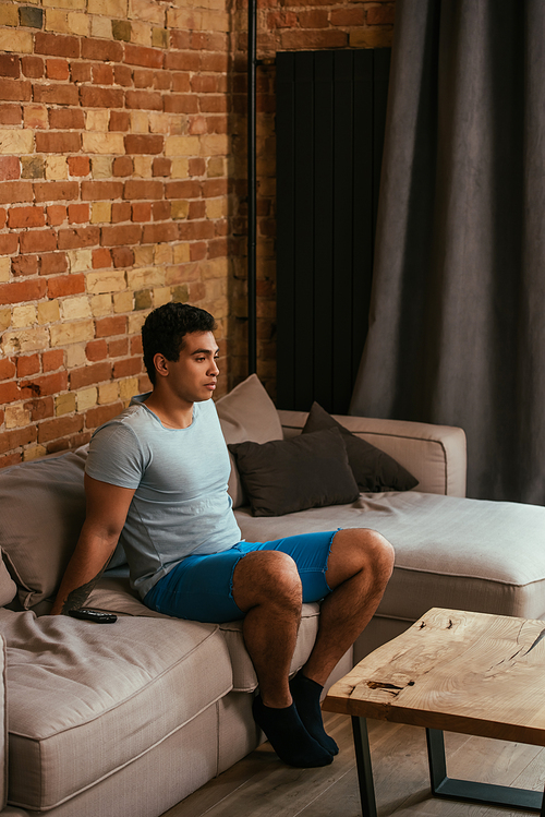 handsome mixed race man sitting on sofa in living room during quarantine