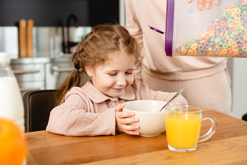 selective focus of mother holding container with delicious corn flakes near bowl and cheerful daughter
