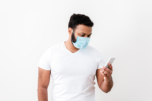 african american man in medical mask using smartphone near white wall