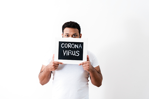 african american man in medical mask covering face with coronavirus lettering on chalkboard near white wall