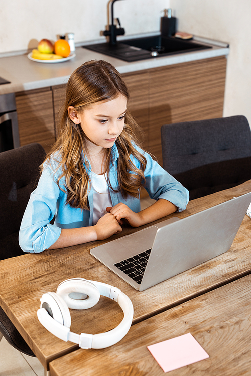 cute kid online studying while looking at laptop near headphones at home