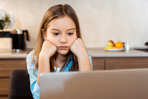 selective focus of bored kid online studying and looking at laptop at home