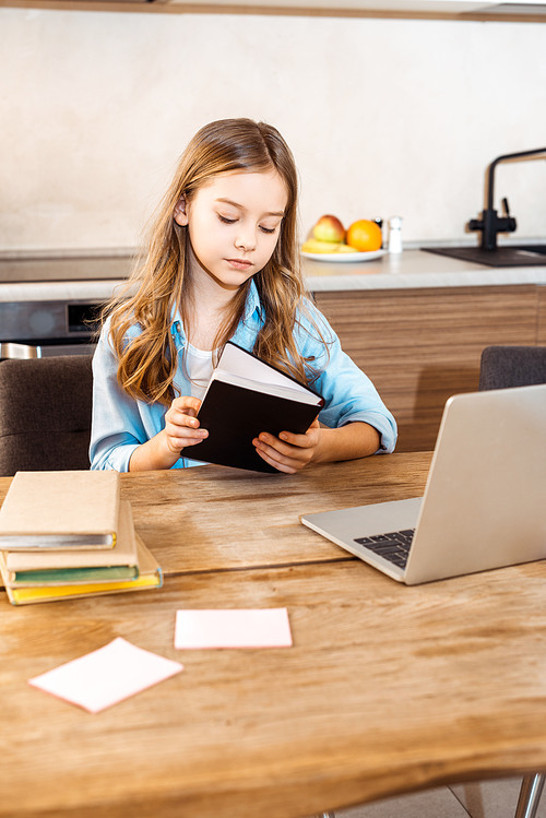 selective focus of kid holding book near laptop while online studying at home