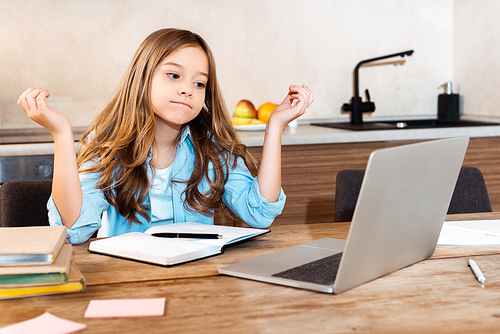 selective focus of confused kid looking at laptop while e-learning at home