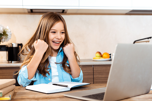 selective focus of excited kid gesturing and looking at laptop while e-learning at home