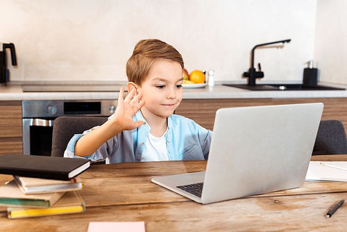 selective focus of cute child waving hand and looking at laptop while e-learning at home