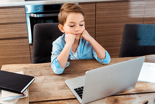 selective focus of bored child looking at laptop while e-learning at home