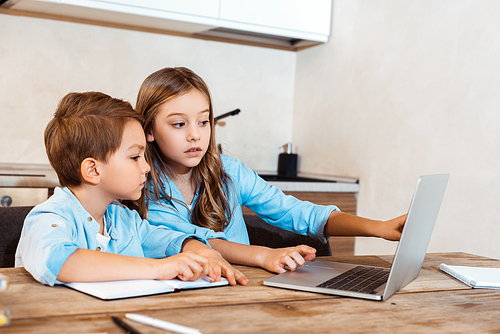 selective focus of sister and brother looking at laptop while e-learning at home