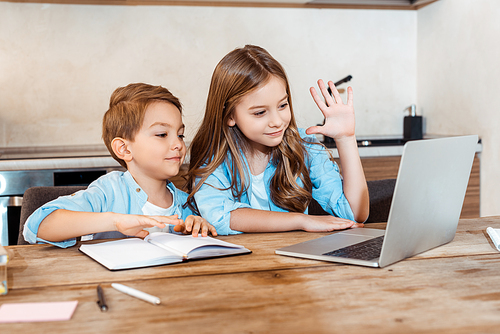 selective focus of happy kid waving hand near brother and having video chat while e-learning at home