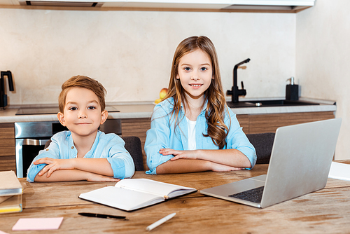 selective focus of happy sister and brother sitting near laptop while e-learning at home