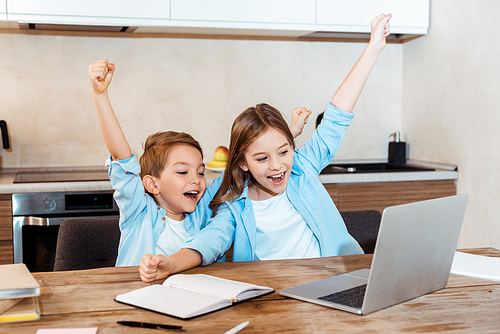 selective focus of happy kids with hands above head looking at laptop while having video chat at home